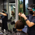 A professional girl hairdresser makes a client haircut. The girl is sitting in a mask in beauty the salon